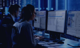 Female working in a Surveillance Team Gives Instructions with the Help of the Headsets. In the Background People Working and Monitors Show Various Information.